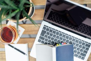 Laptop na biurku, z boku notatki i kubek herbaty
