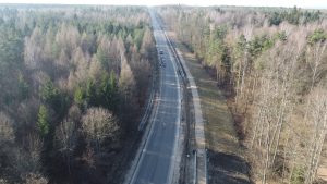Zdjęcie z lotu ptaka pokazujące fragment odnowionej drogi, kilka samochodów już nią jedzie, droga przebiega przez las